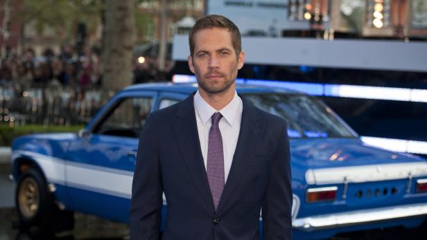 Paul Walker posiert vor einem blauen Auto.