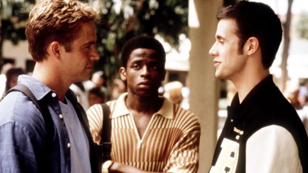 Drei junge Männer stehen im Freien und unterhalten sich.