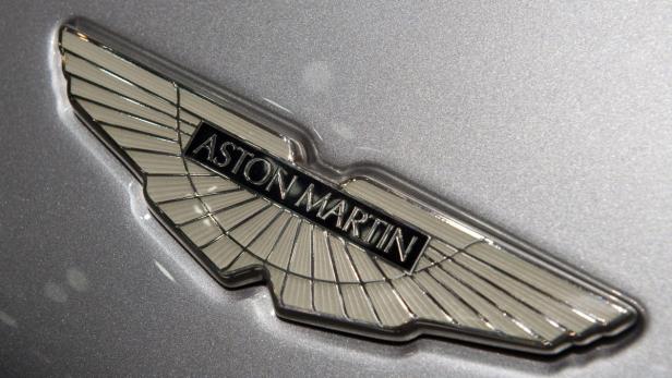 Das geflügelte Logo von Aston Martin auf einem silbernen Auto.