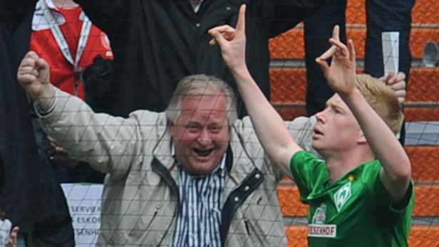 Ein Fußballspieler und ein Fan jubeln mit erhobenen Armen hinter einem Netz.