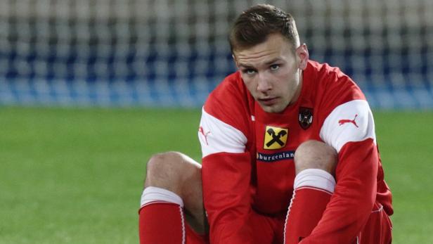 Ein Fußballspieler in roter Spielkleidung sitzt auf dem Rasen.