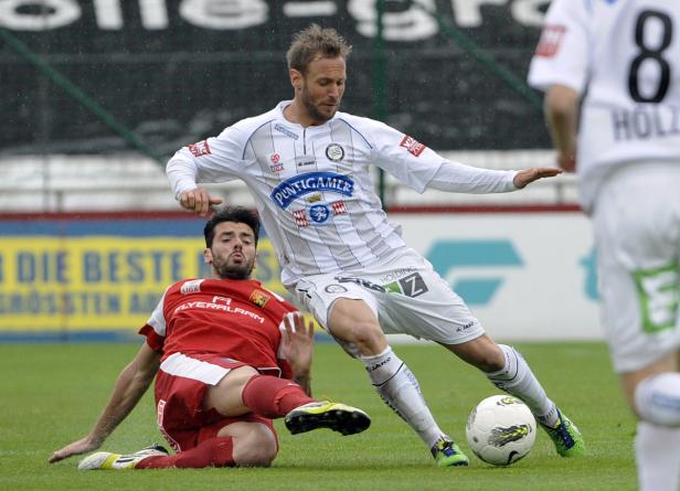 Ein Fußballspieler in Weiß dribbelt den Ball, während ein Gegenspieler in Rot zu Boden geht.