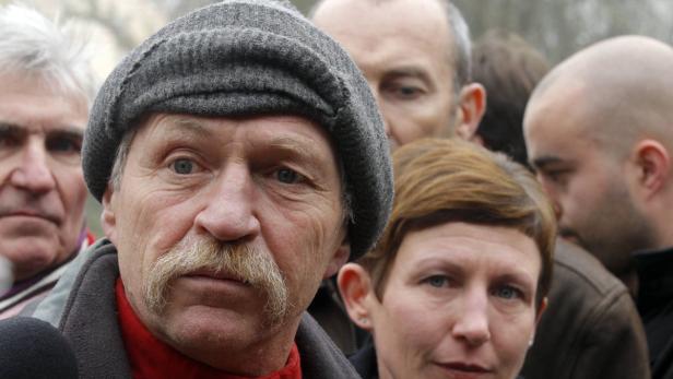 Eine Gruppe von Menschen, darunter ein Mann mit Schnurrbart und Mütze, blickt in die Kamera.