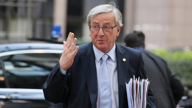 Jean-Claude Juncker winkt mit einer Hand und hält Dokumente.