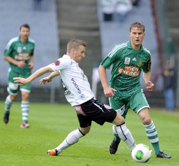 Zwei Fußballspieler kämpfen um den Ball auf einem grünen Rasen.