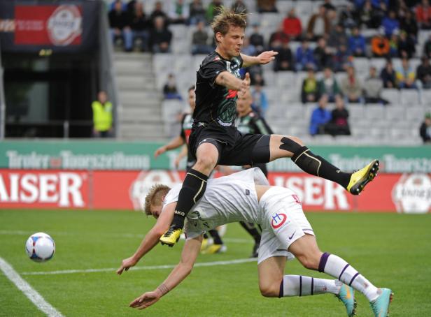 Ein Fußballspieler springt über einen am Boden liegenden Gegenspieler.