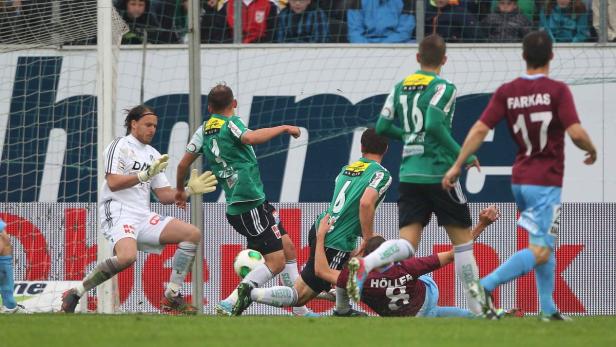 Ein Fußballspiel mit Spielern in grünen und weinroten Trikots in Aktion vor dem Tor.