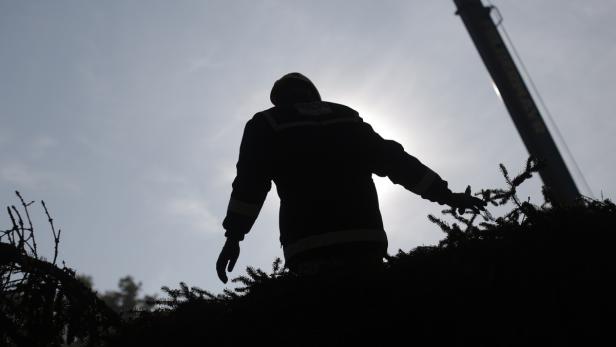 Die Silhouette eines Feuerwehrmanns vor einem hellen Himmel und einem Kranwagen.