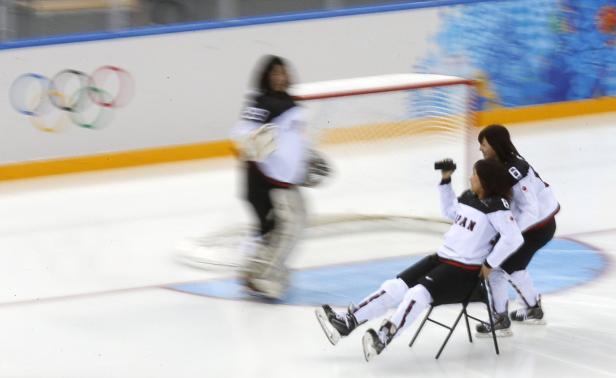 Japanische Eishockeyspielerinnen feiern auf dem Eis, während eine Torhüterin im Hintergrund steht.