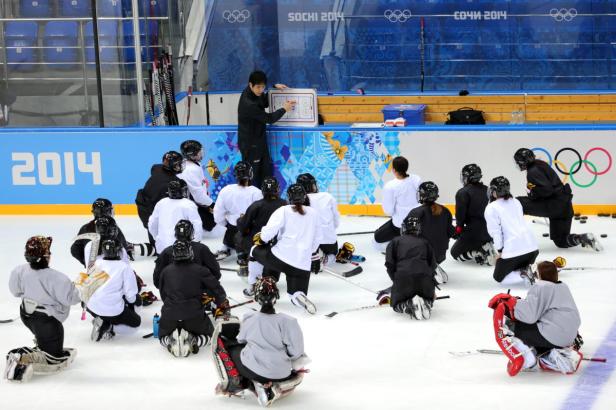 Ein Eishockeytrainer erklärt einer Gruppe von Spielerinnen eine Taktiktafel bei den Olympischen Winterspielen in Sotschi 2014.