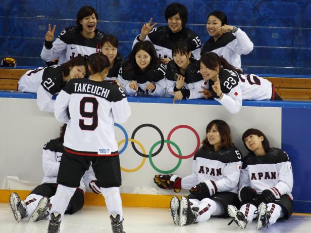 Das japanische Fraueneishockeyteam posiert vor dem Hintergrund der Olympischen Ringe.
