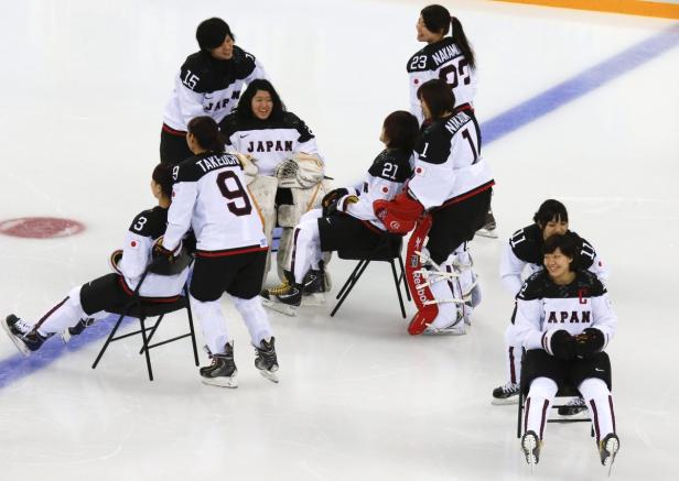 Das japanische Fraueneishockeyteam sitzt und steht auf dem Eis.