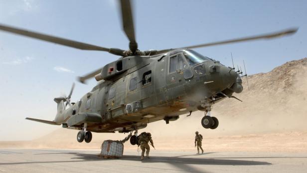 Ein Militärhubschrauber landet in einem Wüstengebiet, während Soldaten eine Ladung sichern.