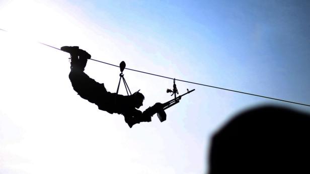 Die Silhouette eines Soldaten, der mit einem Gewehr an einer Seilrutsche hängt.