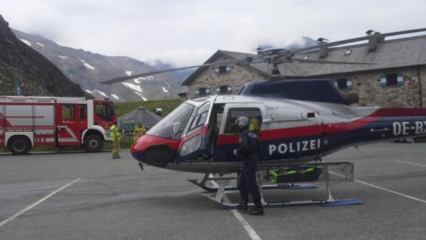 Ein Polizei-Hubschrauber steht neben einem Feuerwehrauto in einer Berglandschaft.