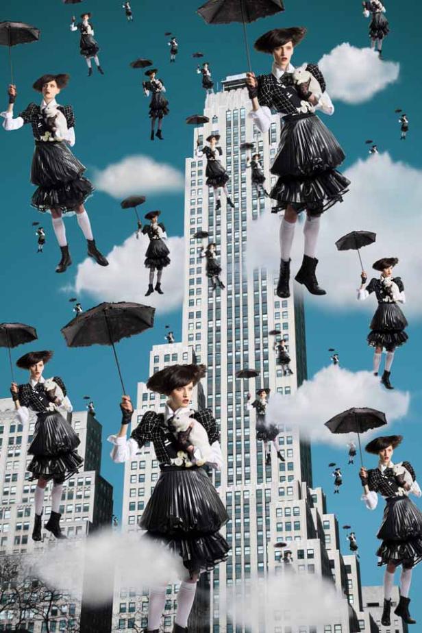 Mehrere Frauen in ungewöhnlicher Kleidung schweben mit Regenschirmen vor einem Wolkenkratzer.