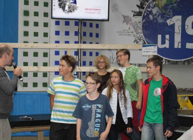 Eine Gruppe von Jugendlichen steht vor einem Mann mit Mikrofon bei einer Veranstaltung von Ars Electronica.