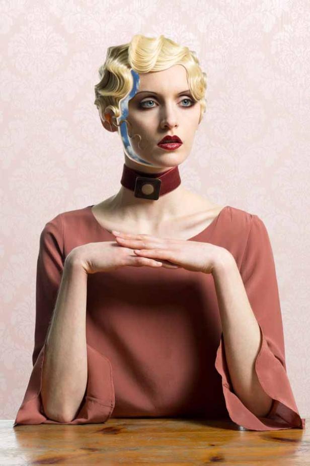 Eine Frau mit blondem Haar im Stil der 1920er Jahre und einem roten Choker blickt nachdenklich zur Seite.