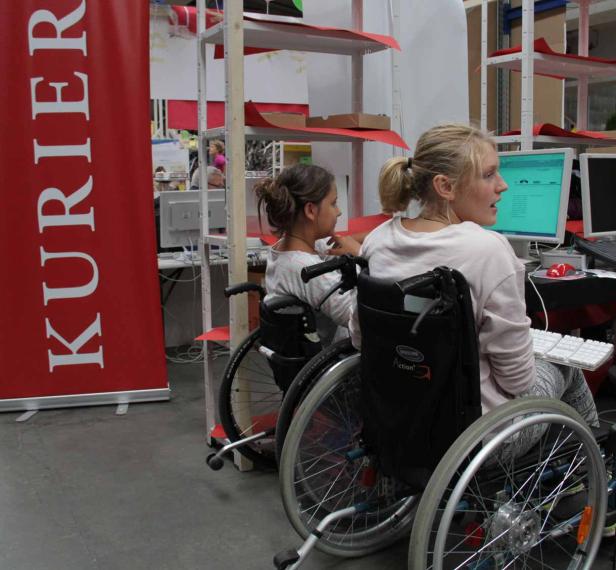 Zwei junge Frauen im Rollstuhl sitzen vor Computern auf einer Veranstaltung des „Kurier“.
