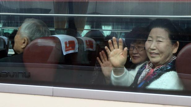 Ältere Menschen winken aus dem Fenster eines Busses.