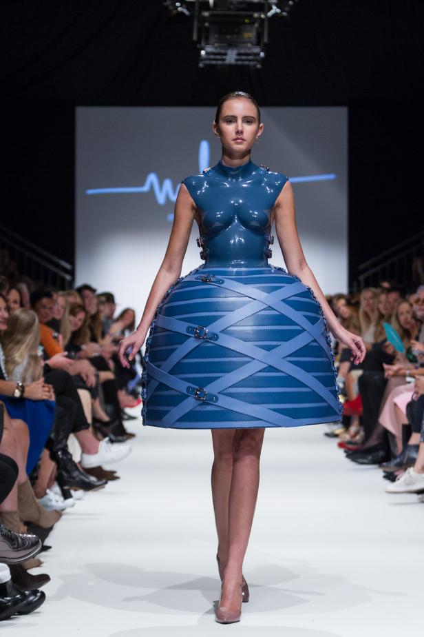 Eine Frau präsentiert ein blaues Kleid mit ungewöhnlichem Design auf einem Laufsteg.