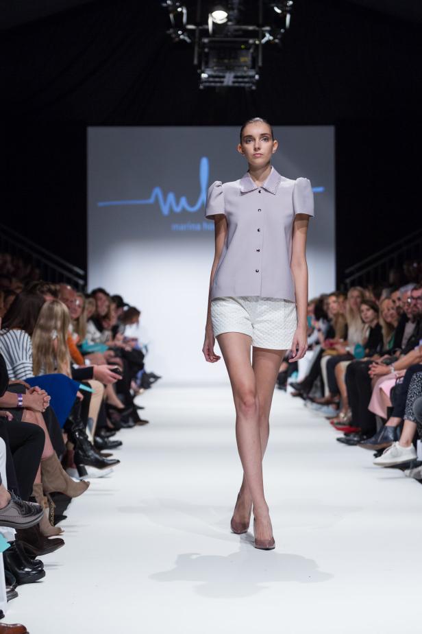 Eine Frau präsentiert Mode auf einem Laufsteg vor Publikum.