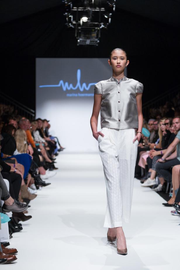 Eine junge Frau präsentiert ein silbernes Oberteil und eine weiße Hose auf einem Laufsteg.