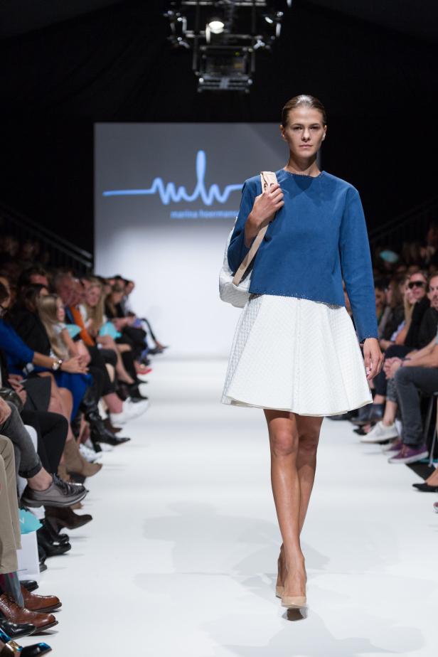 Eine Frau präsentiert ein blaues Oberteil und einen weißen Rock auf dem Laufsteg.