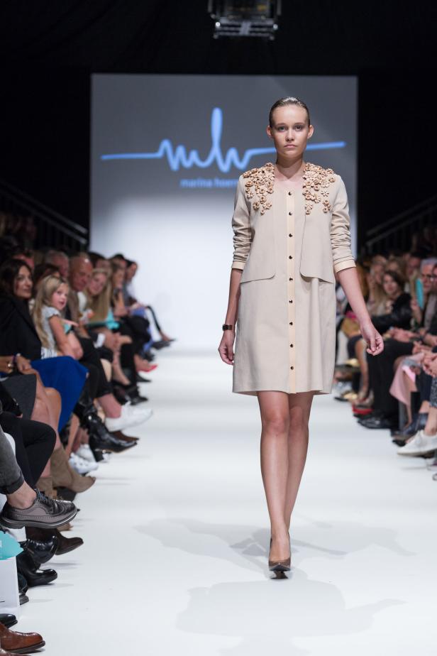 Ein Model präsentiert ein beiges Kleid mit floralen Applikationen auf einem Laufsteg.