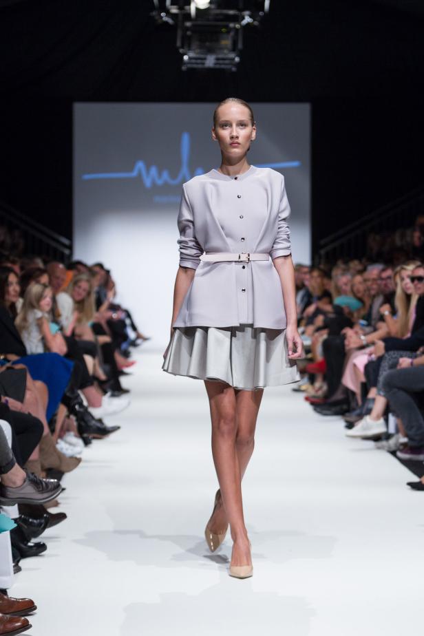 Eine Frau präsentiert ein helles Kleid mit Gürtel auf einem Laufsteg.