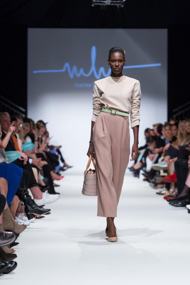 Eine dunkelhäutige Frau präsentiert ein beiges Outfit mit Handtasche auf dem Laufsteg.