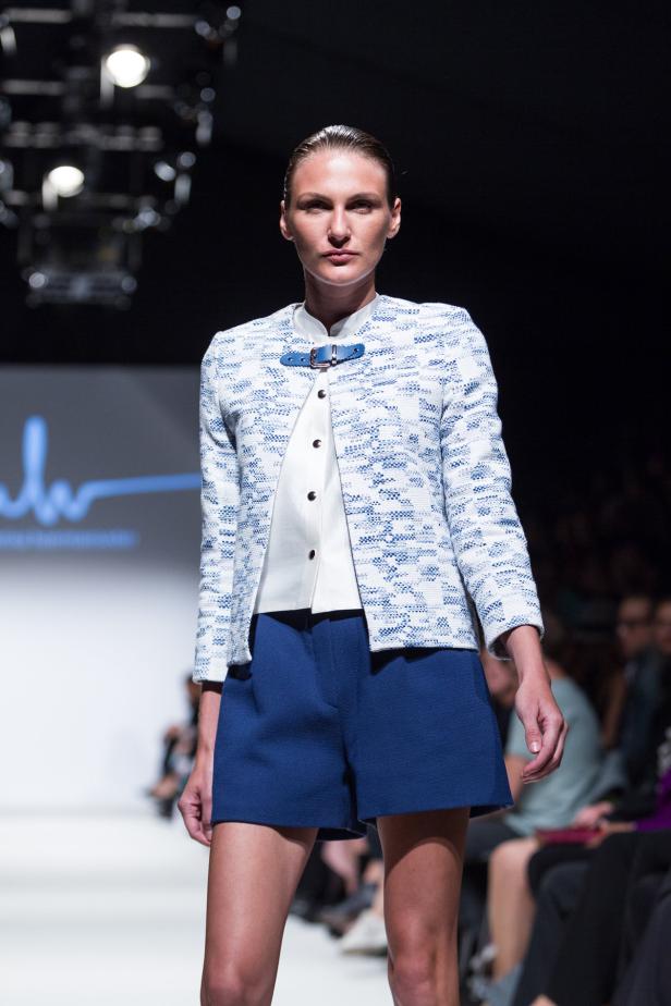 Eine Frau präsentiert eine Jacke mit blauen Shorts auf einem Laufsteg.