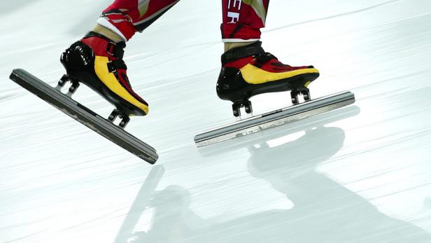Ein Eisschnellläufer mit rot-gelb-schwarzen Schlittschuhen auf einer Eisbahn.