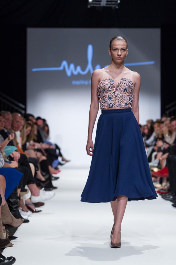 Ein Model läuft auf dem Laufsteg in einem blauen Rock und einem verzierten Oberteil.