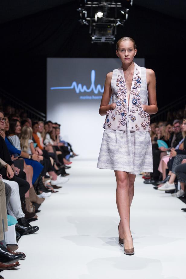 Ein Model präsentiert ein ärmelloses Kleid mit floralen Applikationen auf einem Laufsteg.