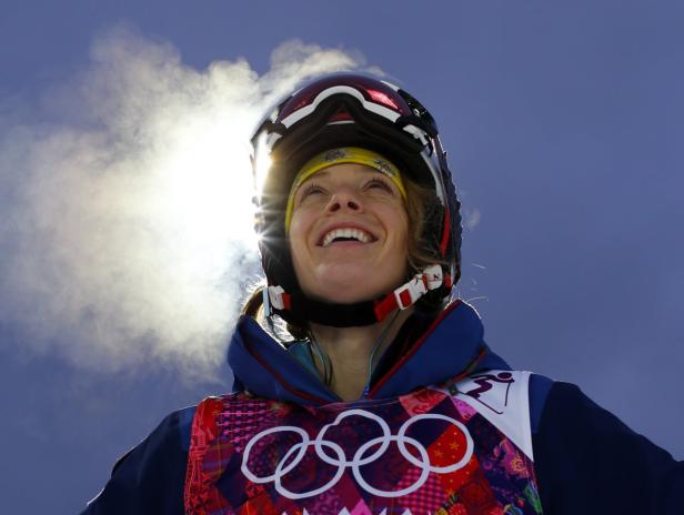 Eine lächelnde Skifahrerin mit Helm und gelbem Stirnband blickt in den Himmel.