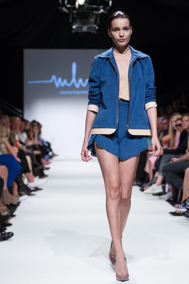 Eine Frau präsentiert ein blaues Hosen- und Jacken-Ensemble auf dem Laufsteg.