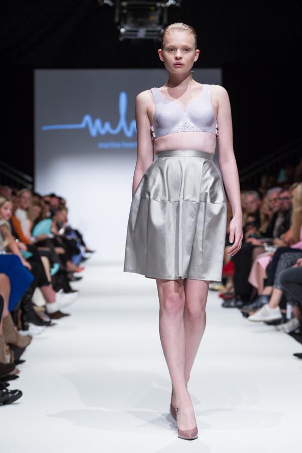 Ein Model präsentiert ein silbernes Outfit auf einem Laufsteg.