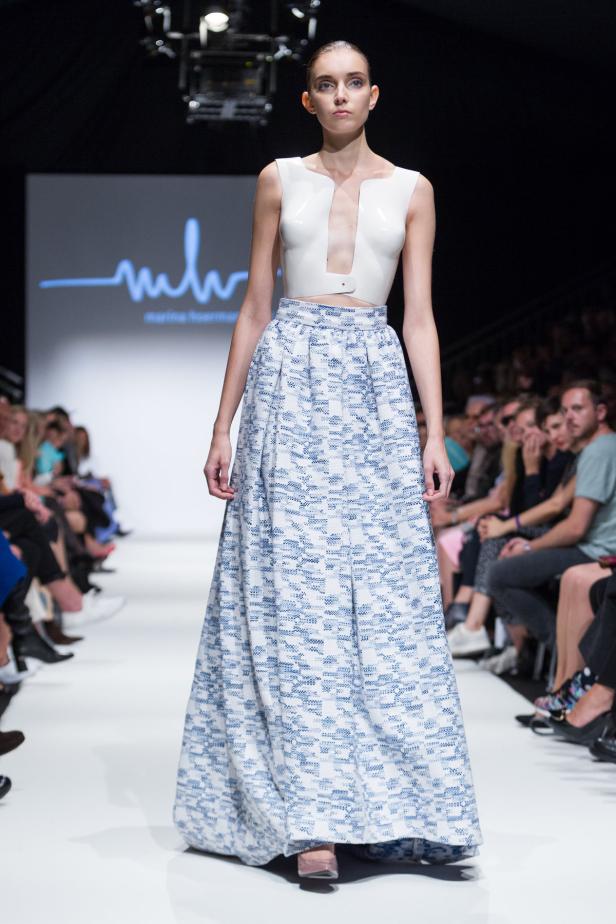Eine Frau präsentiert ein weißes Oberteil und einen langen, blau gemusterten Rock auf dem Laufsteg.