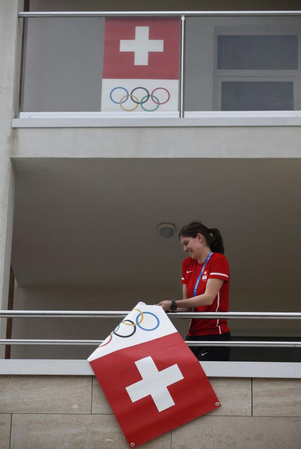 Eine Frau auf einem Balkon mit einer Schweizer Flagge und den Olympischen Ringen.