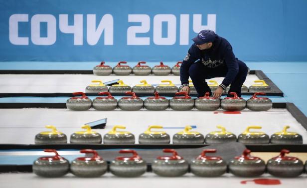 Ein Mann hockt auf einer Eisbahn vor Curlingsteinen bei den Olympischen Winterspielen in Sotschi 2014.