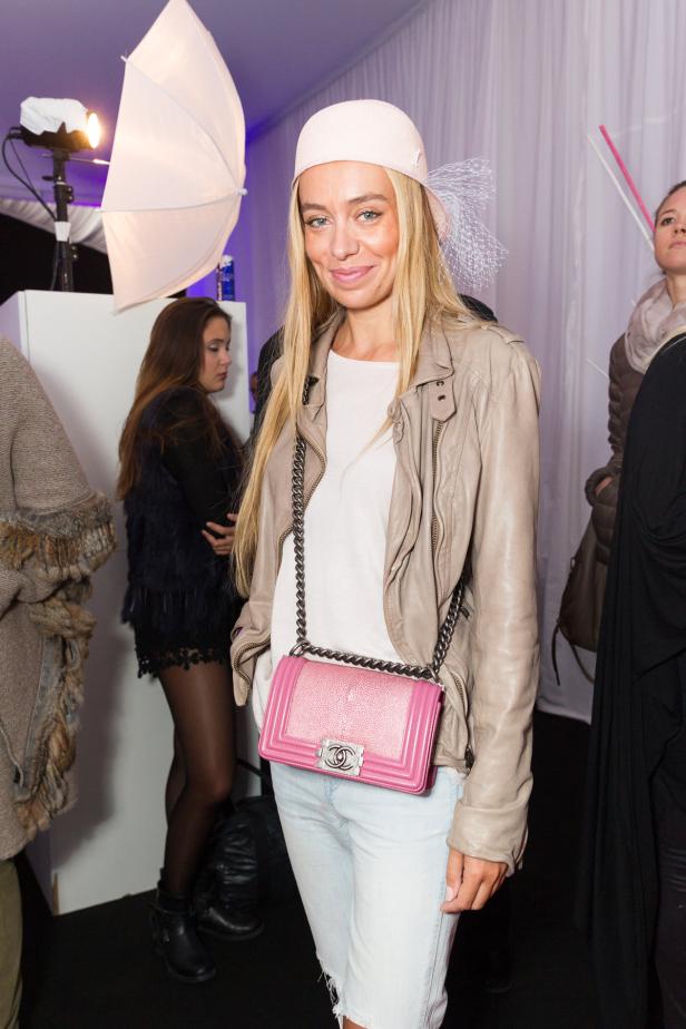 Eine Frau mit hellblonden Haaren, beiger Jacke und rosa Chanel-Tasche posiert.