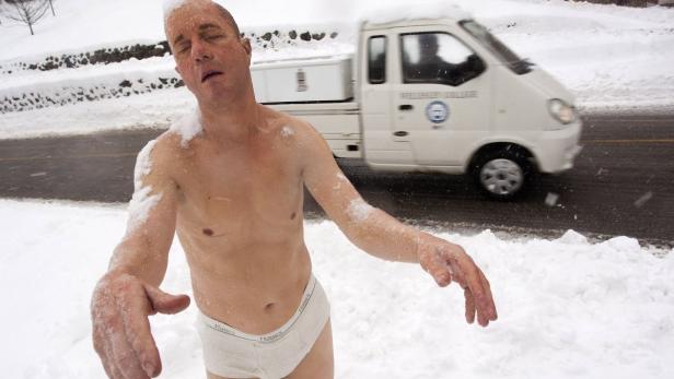 Ein Mann, nur mit Unterwäsche bekleidet, steht im Schnee, während ein Lieferwagen vorbeifährt.