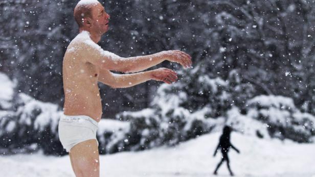 Ein Mann in Unterwäsche steht im Schnee, während es schneit.