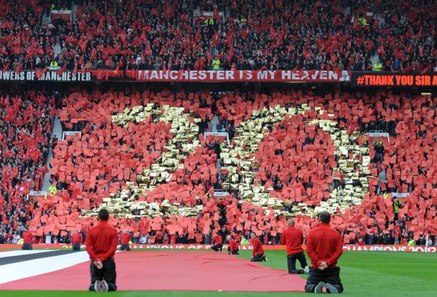 Volles Fußballstadion mit roter und goldener Choreografie und Bannern.