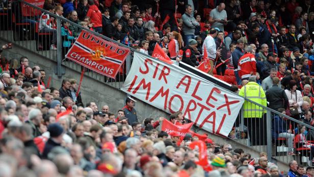 Fußballfans halten ein Banner mit der Aufschrift „Sir Alex Immortal“ im Stadion.