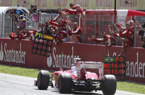 Ein roter Formel-1-Rennwagen fährt an einer jubelnden Boxenmannschaft vorbei.