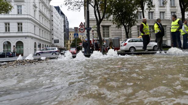 Überschwemmte Straße in Wien mit Einsatzkräften und einem Polizeiauto.