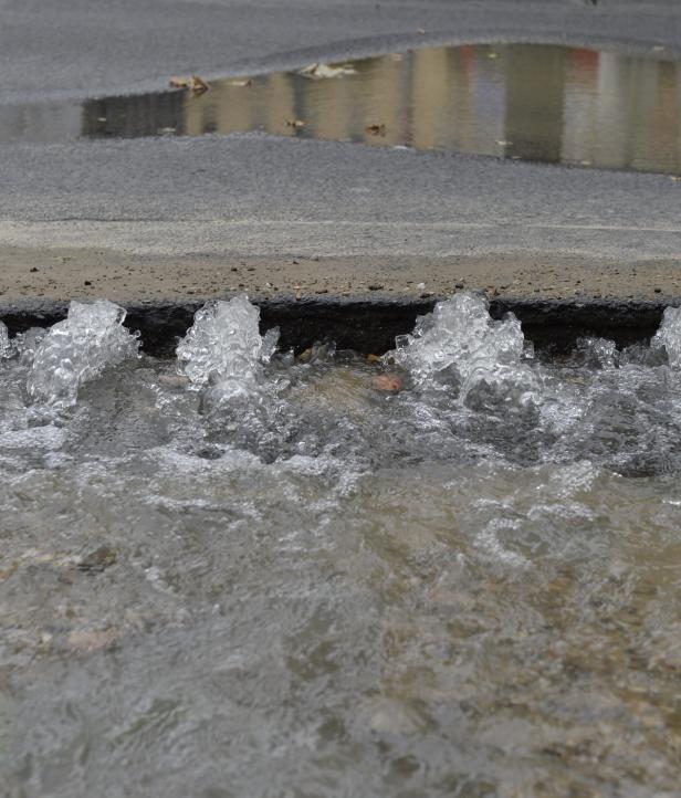 Wasser fließt in einen Straßenablauf.