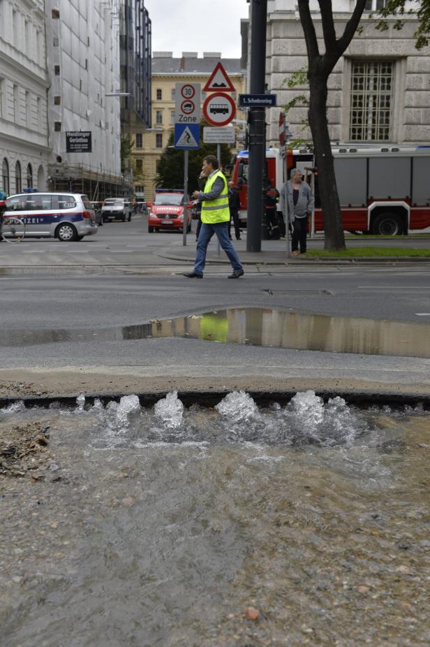 Ein Wasserrohrbruch auf einer Straße in Wien, im Hintergrund ein Feuerwehrauto.
